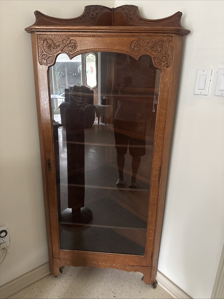 This is a Victorian-style oak curio cabinet carved top and a single glass door